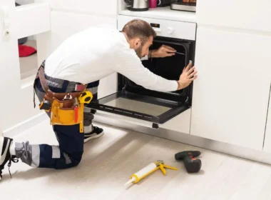 Køkkenrenovering i gang. Håndværker monterer ny ovn med professionelt værktøj i renoveret køkken med hvide skabe