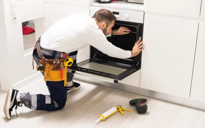 Køkkenrenovering i gang. Håndværker monterer ny ovn med professionelt værktøj i renoveret køkken med hvide skabe